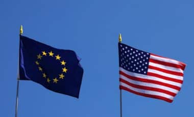 Les drapeaux de l’Union européenne et des États-Unis flottent côte à côte, illustrant les tensions commerciales liées aux droits de douane.