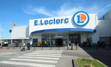 Un supermarché Leclerc avec des clients entrant et sortant sous un ciel ensoleillé.