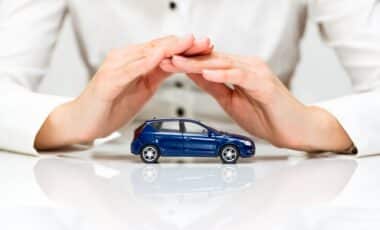 L’image montre une voiture miniature protégée par les mains d’une personne, illustrant le concept de protection et d’assurance automobile.