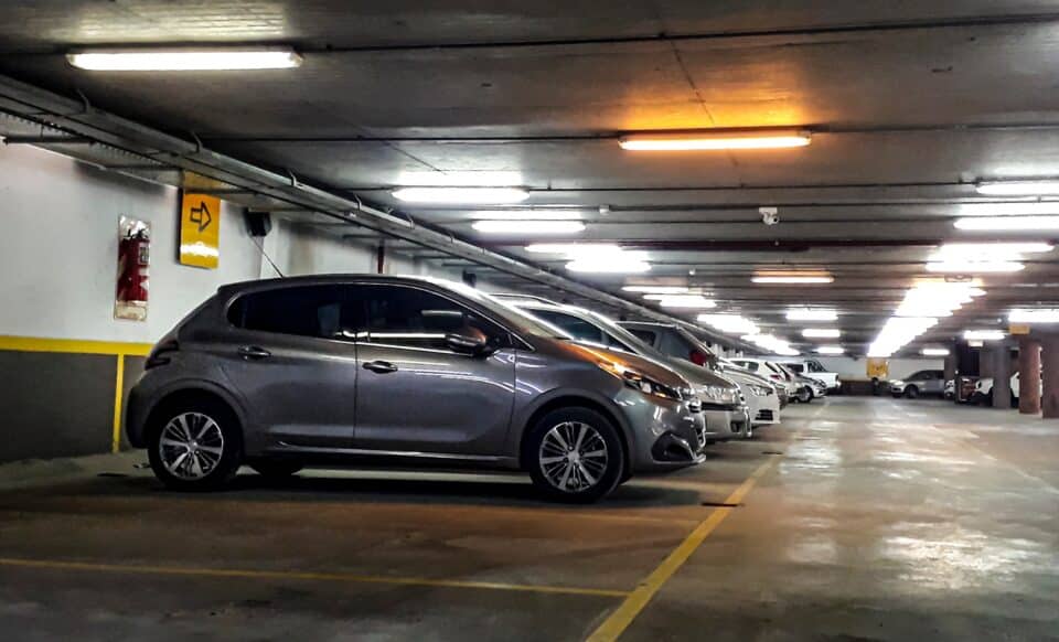 Parking souterrain éclairé avec plusieurs voitures alignées, ambiance sécurisée mais légèrement vieillissante.