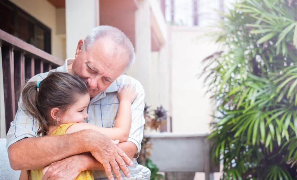 Un grand-père retraité serre affectueusement sa petite-fille dans ses bras, illustrant le lien intergénérationnel et l’importance de la retraite pour profiter de sa famille.