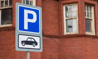 Un panneau de stationnement indiquant une zone de parking réservé aux voitures, installé devant un bâtiment en briques.