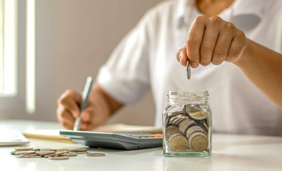 Image d'une personne qui dépose des pièces dans un bocal pour illustrer l'épargne salariale