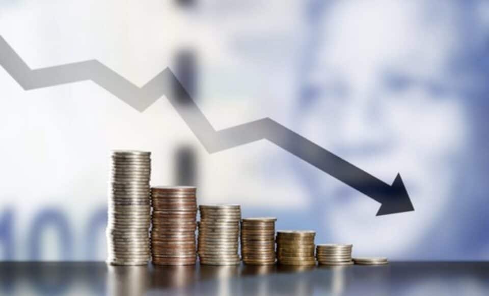 L'image montre des piles de pièces de monnaie accompagnées d'une flèche pointant vers le bas, symbolisant la déflation et la baisse de la valeur des actifs.